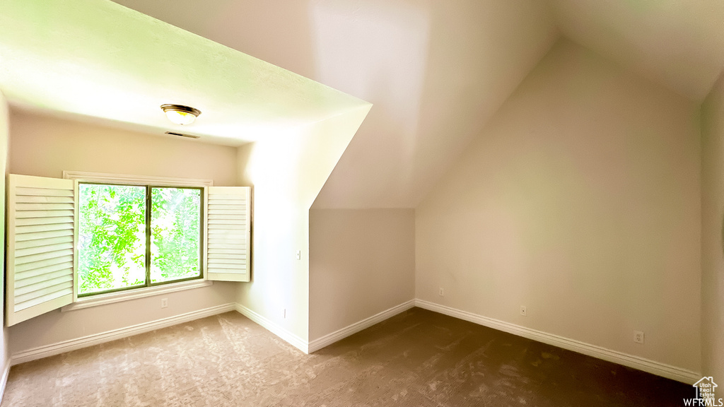 Bonus room with lofted ceiling and dark colored carpet