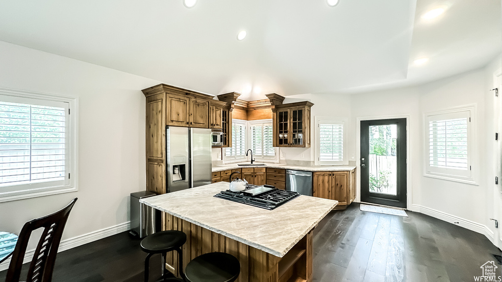 Kitchen with dark hardwood / wood-style flooring, appliances with stainless steel finishes, light stone counters, a breakfast bar area, and sink