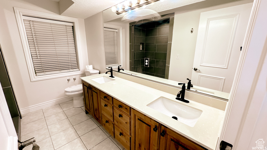 Bathroom featuring tile flooring, a textured ceiling, double vanity, and toilet