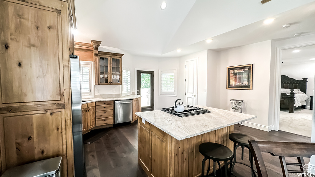 Kitchen featuring appliances with stainless steel finishes, light stone counters, dark hardwood / wood-style floors, a kitchen bar, and a center island