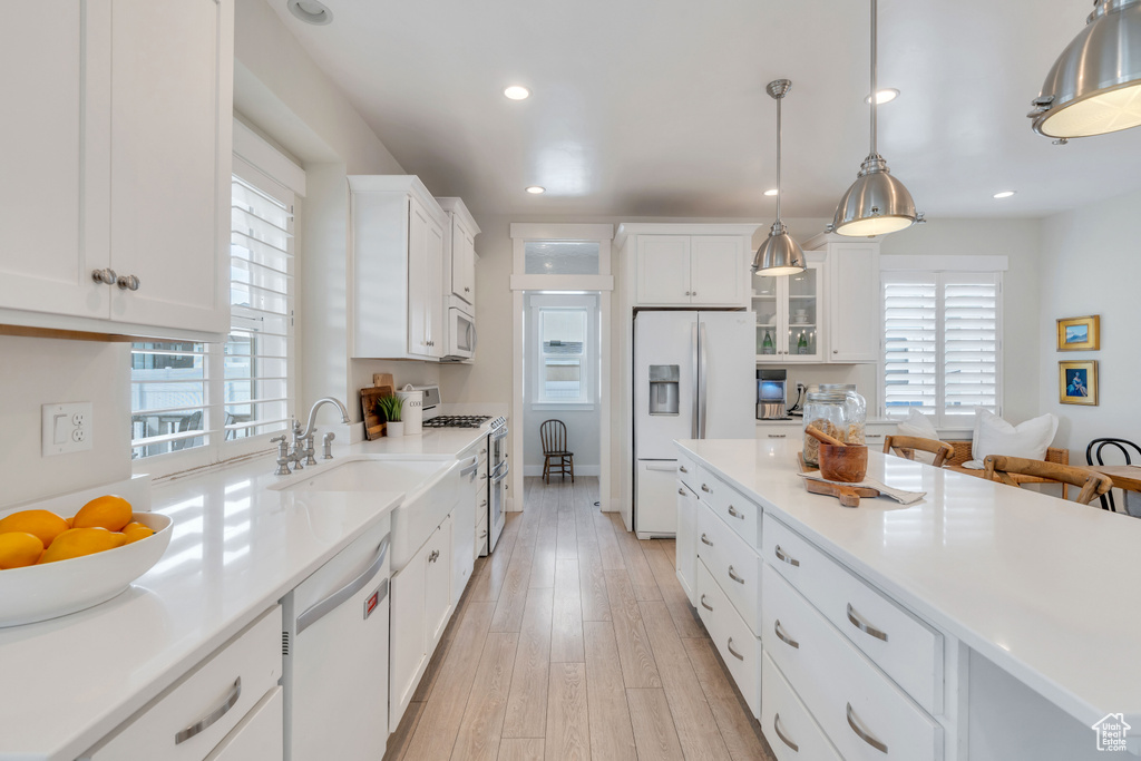 Kitchen with white appliances, plenty of natural light, white cabinetry, and hanging light fixtures
