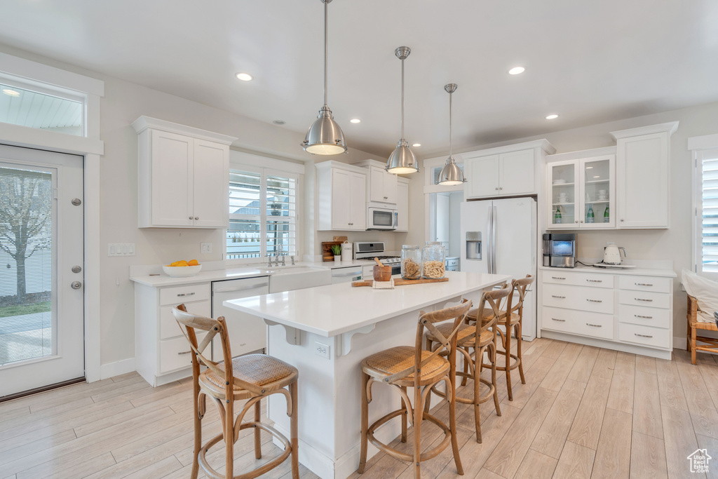 Kitchen featuring a kitchen island, light hardwood / wood-style floors, white appliances, and white cabinets