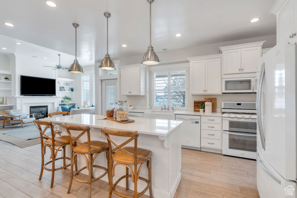 Kitchen featuring white appliances, white cabinetry, light hardwood / wood-style floors, and a kitchen breakfast bar