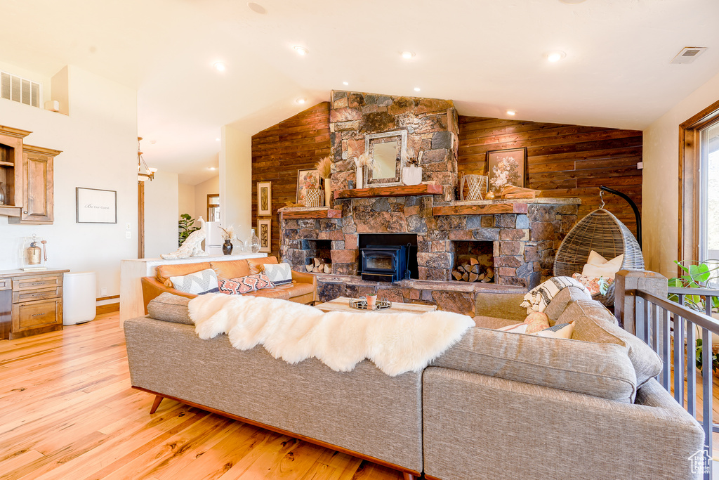 Living room featuring vaulted ceiling, a fireplace, wood walls, and light wood-type flooring