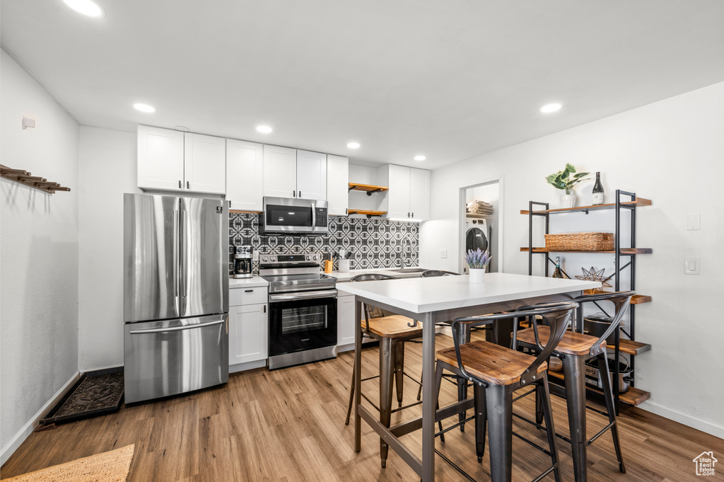 Kitchen with white cabinets, appliances with stainless steel finishes, light hardwood / wood-style floors, and tasteful backsplash