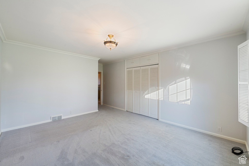 Unfurnished bedroom featuring light colored carpet, a closet, and crown molding