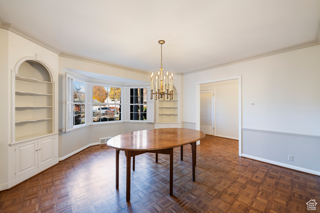 Unfurnished dining area with a notable chandelier, dark parquet floors, crown molding, and built in shelves