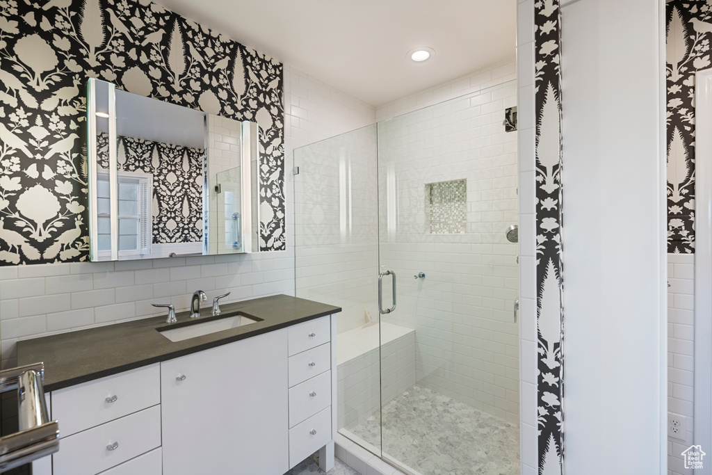 Bathroom featuring a shower with door, tasteful backsplash, vanity, and tile walls