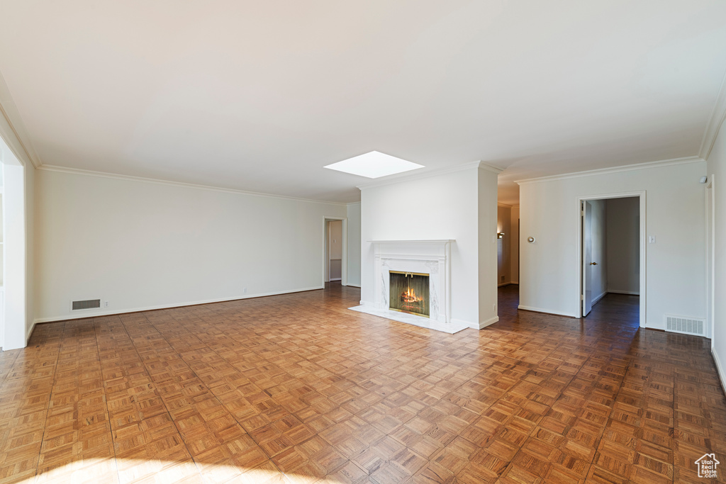 Unfurnished living room featuring a skylight, a fireplace, ornamental molding, and dark parquet flooring