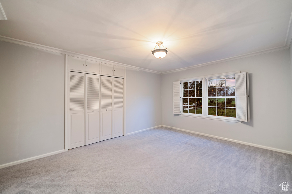 Unfurnished bedroom with crown molding, a closet, and light carpet