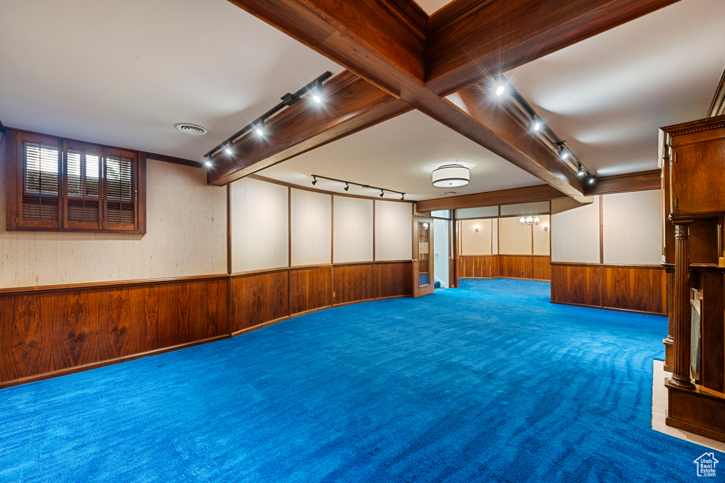Interior space with wooden walls, track lighting, beam ceiling, and dark colored carpet