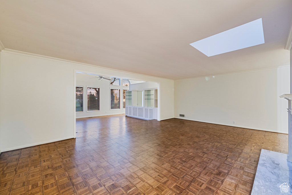 Unfurnished living room with dark parquet floors, crown molding, ceiling fan, and a skylight