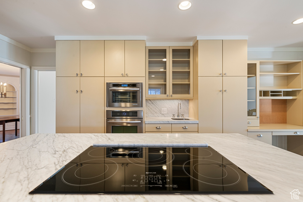 Kitchen featuring cream cabinetry, double oven, black electric cooktop, and light stone counters