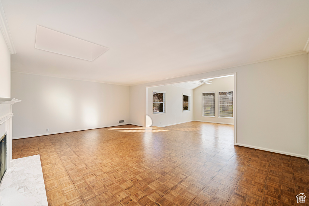 Unfurnished living room with ceiling fan, ornamental molding, and parquet floors