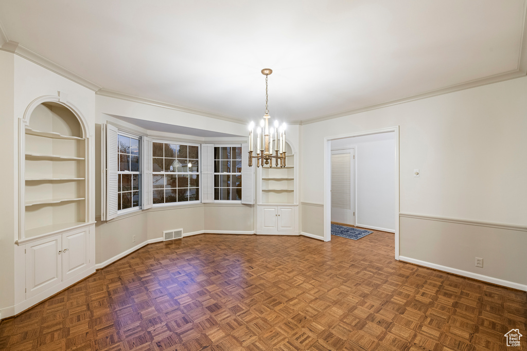 Unfurnished room featuring built in shelves, dark parquet floors, and a chandelier