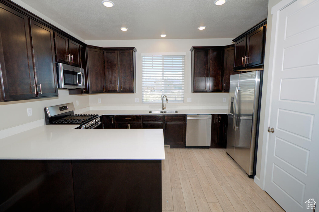 Kitchen with kitchen peninsula, dark brown cabinets, appliances with stainless steel finishes, and sink