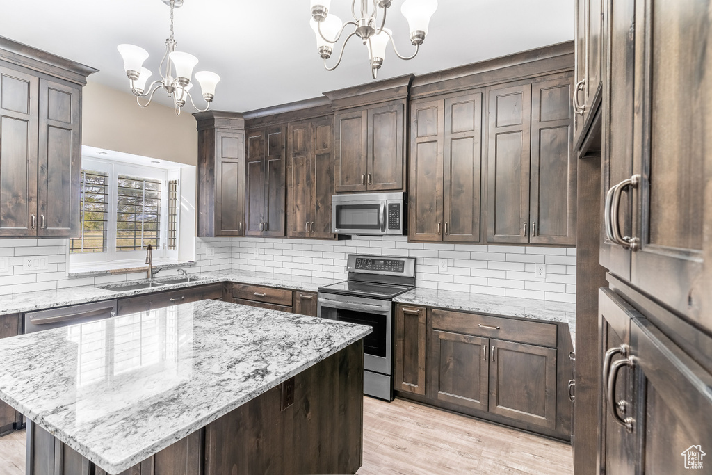 Kitchen featuring a notable chandelier, backsplash, appliances with stainless steel finishes, and a center island