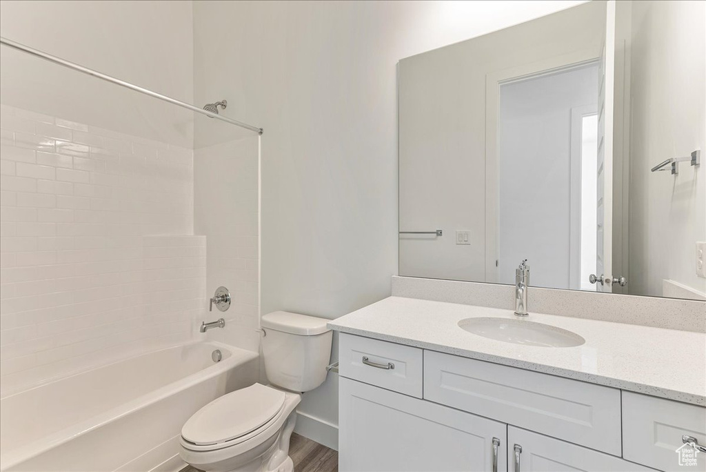Full bathroom with tiled shower / bath combo, toilet, hardwood / wood-style flooring, and vanity with extensive cabinet space