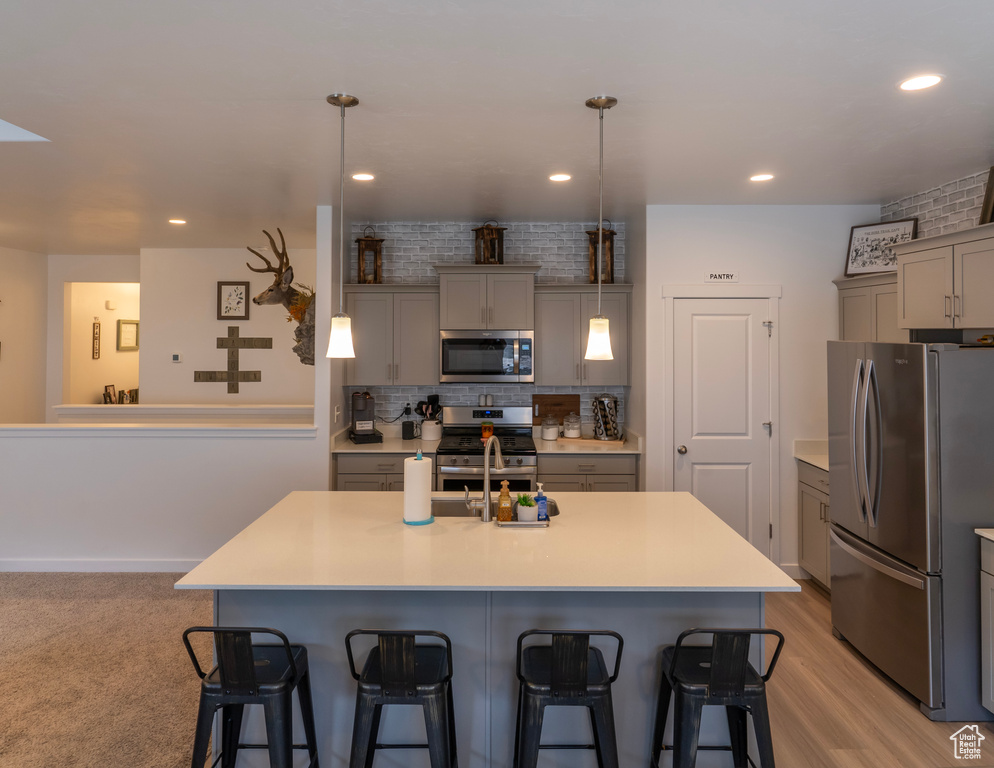 Kitchen featuring pendant lighting, stainless steel appliances, light wood-type flooring, and an island with sink