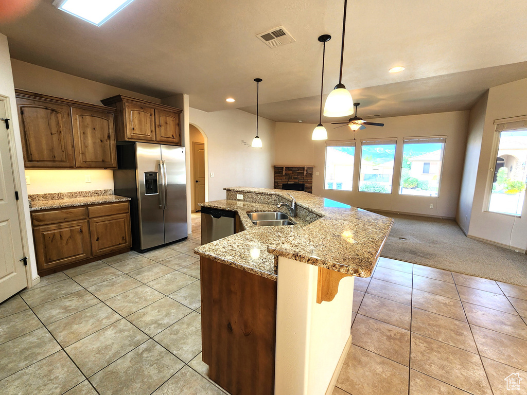 Kitchen featuring decorative light fixtures, ceiling fan, stainless steel appliances, a center island with sink, and light colored carpet