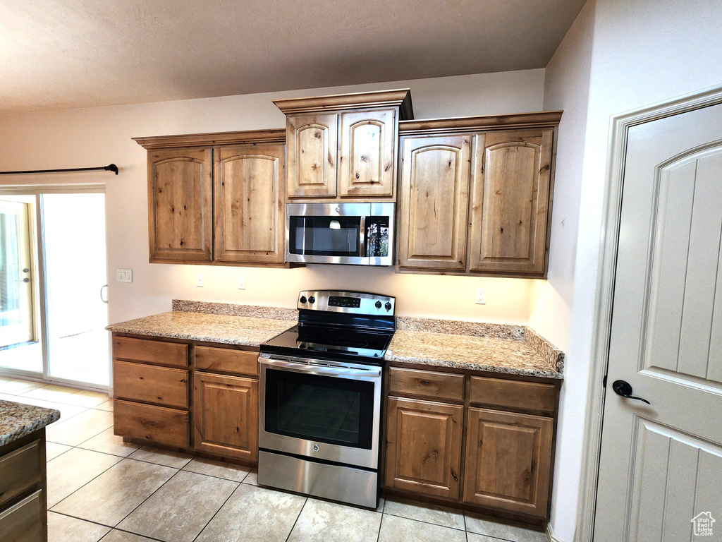 Kitchen featuring appliances with stainless steel finishes, light stone counters, and light tile flooring