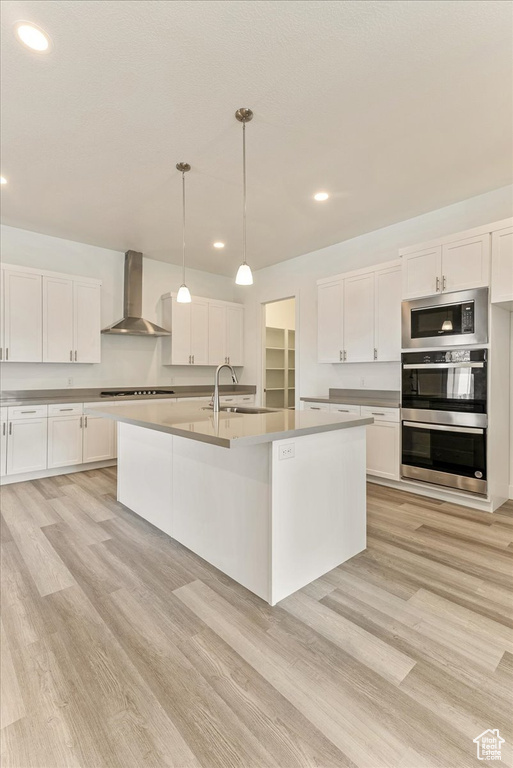 Kitchen featuring stainless steel appliances, light hardwood / wood-style flooring, wall chimney exhaust hood, and white cabinetry