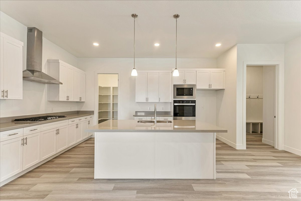 Kitchen with wall chimney range hood, stainless steel appliances, white cabinets, and a kitchen island with sink