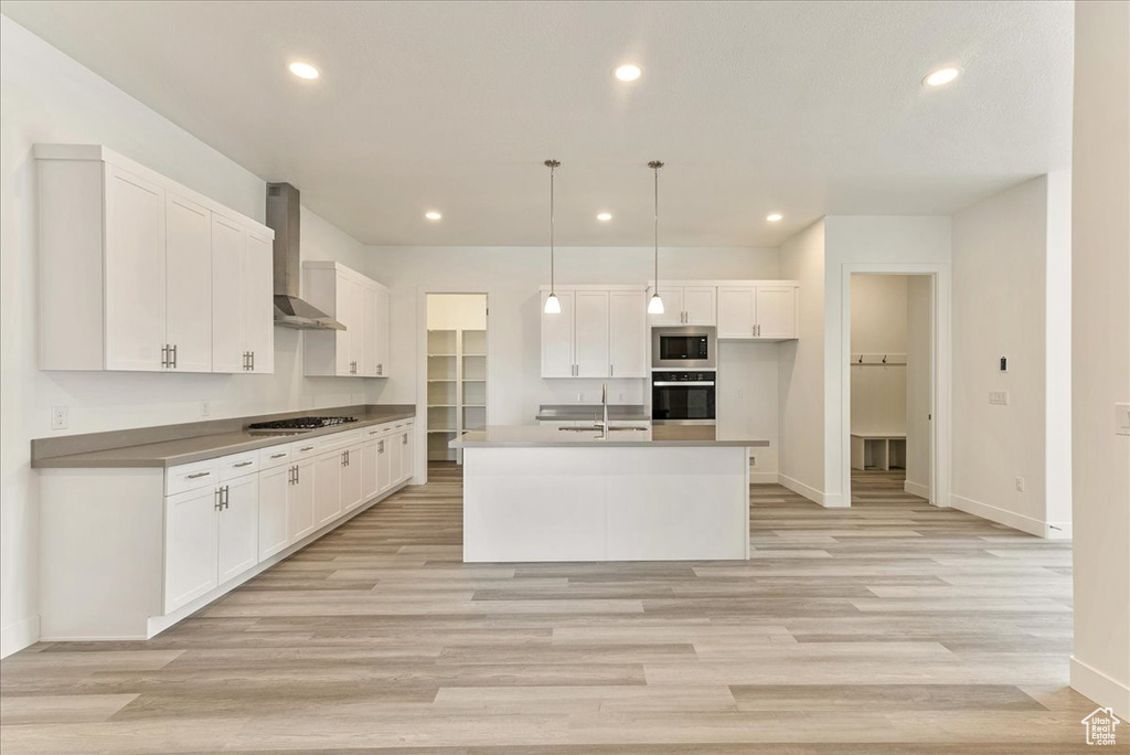 Kitchen with white cabinetry, light hardwood / wood-style flooring, and wall chimney exhaust hood