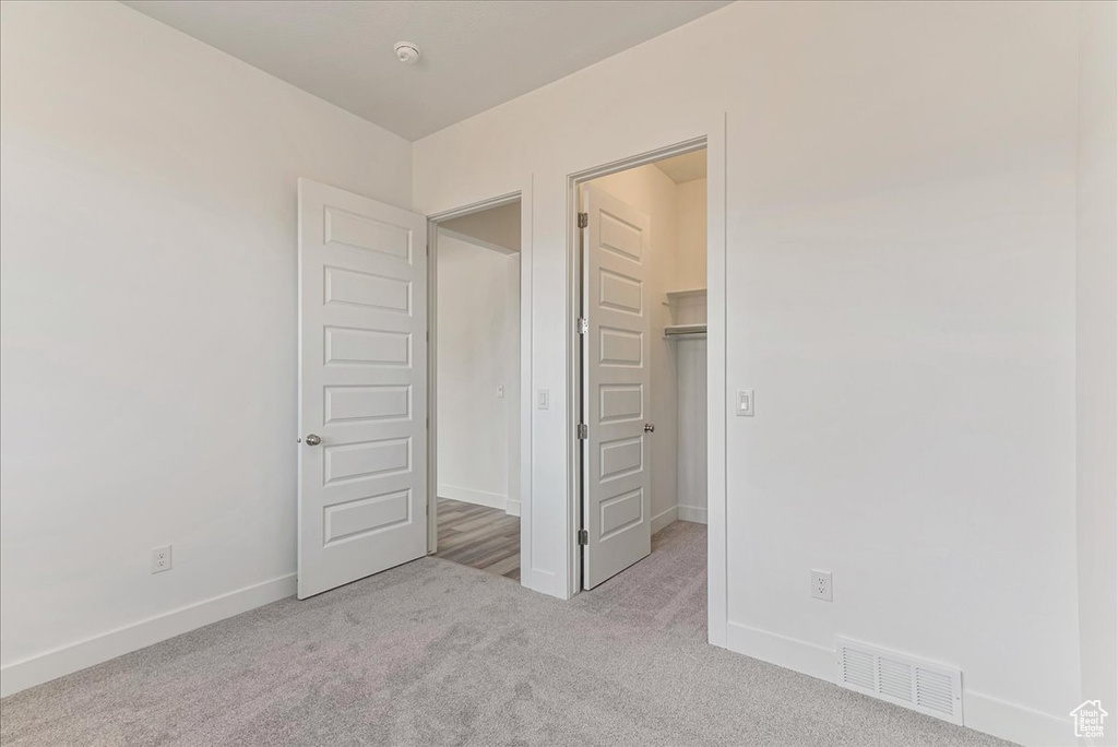 Unfurnished bedroom featuring a closet, light colored carpet, and a spacious closet