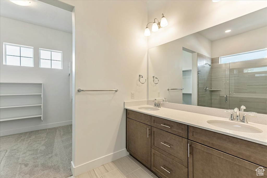 Bathroom with tile flooring, dual sinks, a shower with door, and vanity with extensive cabinet space