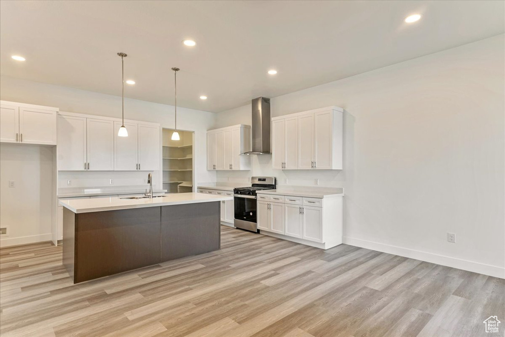 Kitchen featuring white cabinets, light hardwood / wood-style flooring, stainless steel gas range oven, and wall chimney exhaust hood