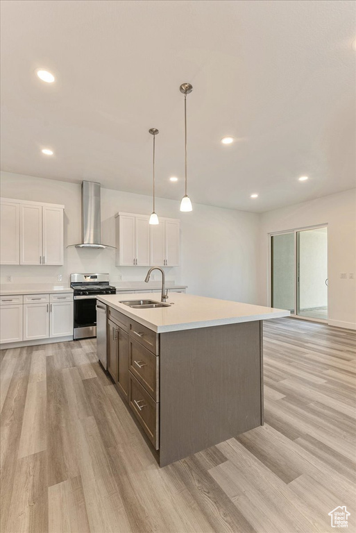 Kitchen featuring appliances with stainless steel finishes, light hardwood / wood-style floors, white cabinetry, wall chimney range hood, and sink