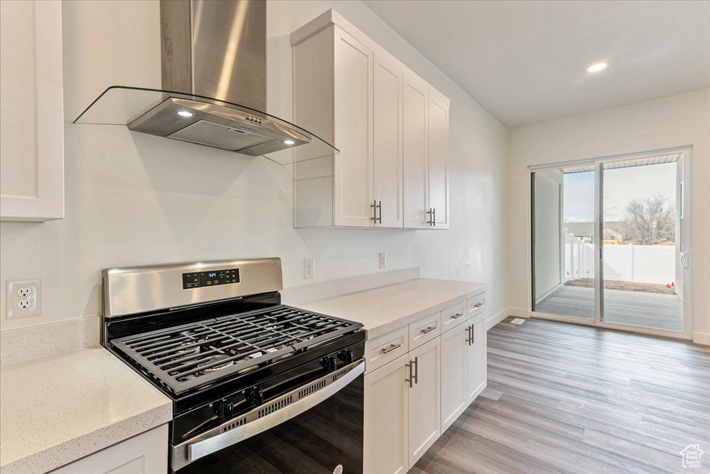 Kitchen featuring light stone countertops, white cabinetry, stainless steel gas range, light hardwood / wood-style floors, and wall chimney exhaust hood