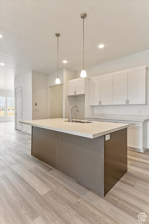 Kitchen featuring white cabinets, light hardwood / wood-style flooring, an island with sink, and pendant lighting