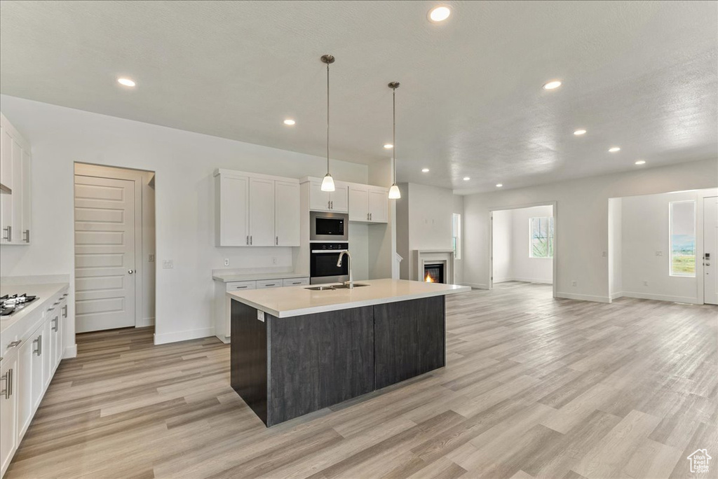 Kitchen featuring pendant lighting, light hardwood / wood-style floors, appliances with stainless steel finishes, white cabinetry, and a kitchen island with sink