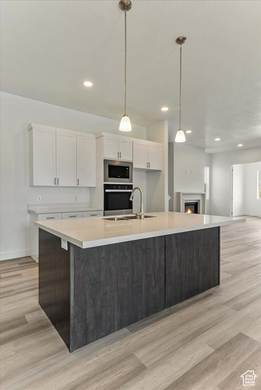 Kitchen featuring a kitchen island with sink, white cabinets, appliances with stainless steel finishes, and light wood-type flooring
