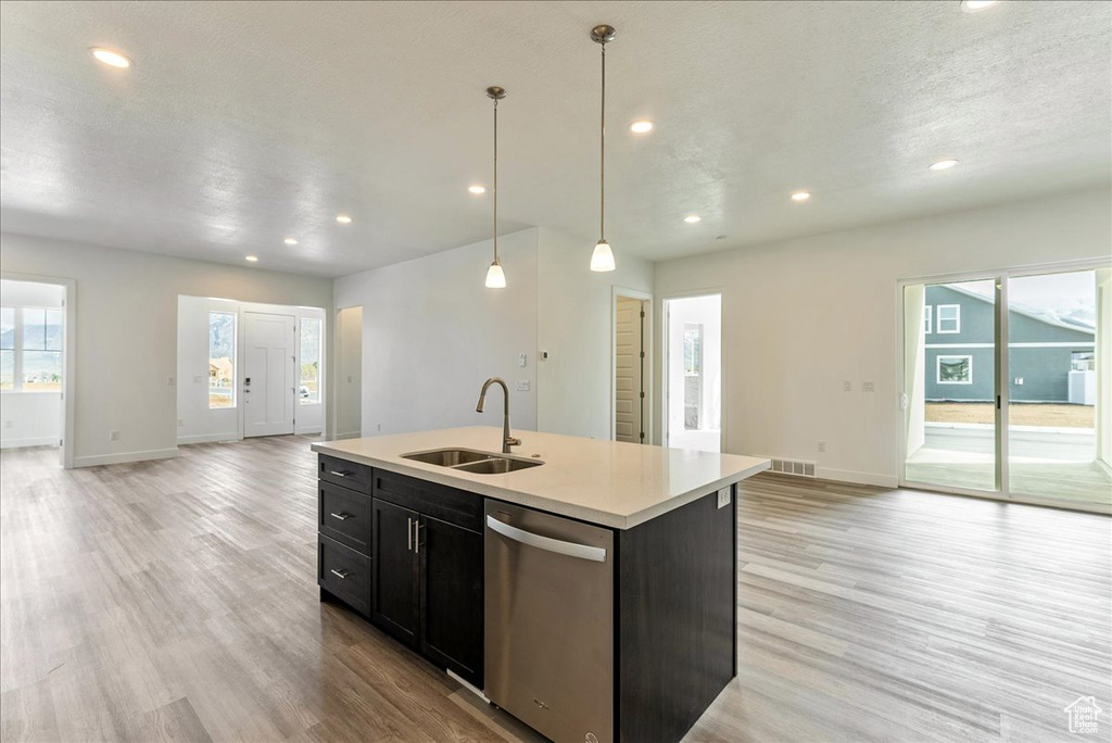 Kitchen with stainless steel dishwasher, pendant lighting, sink, light hardwood / wood-style flooring, and a center island with sink