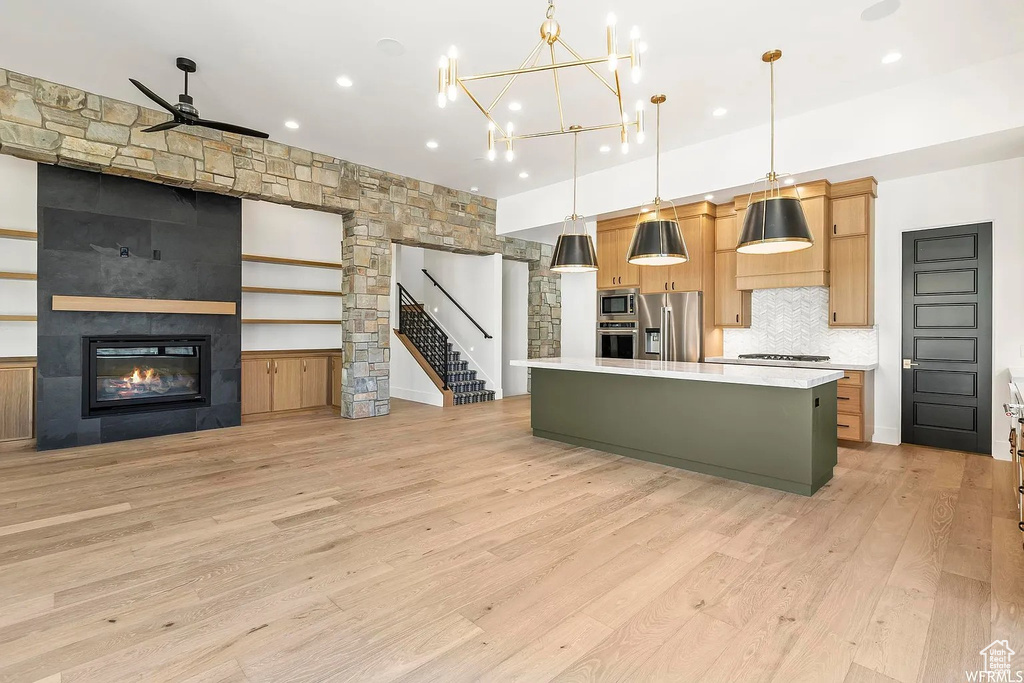 Kitchen featuring appliances with stainless steel finishes, light wood-type flooring, a center island, and a fireplace