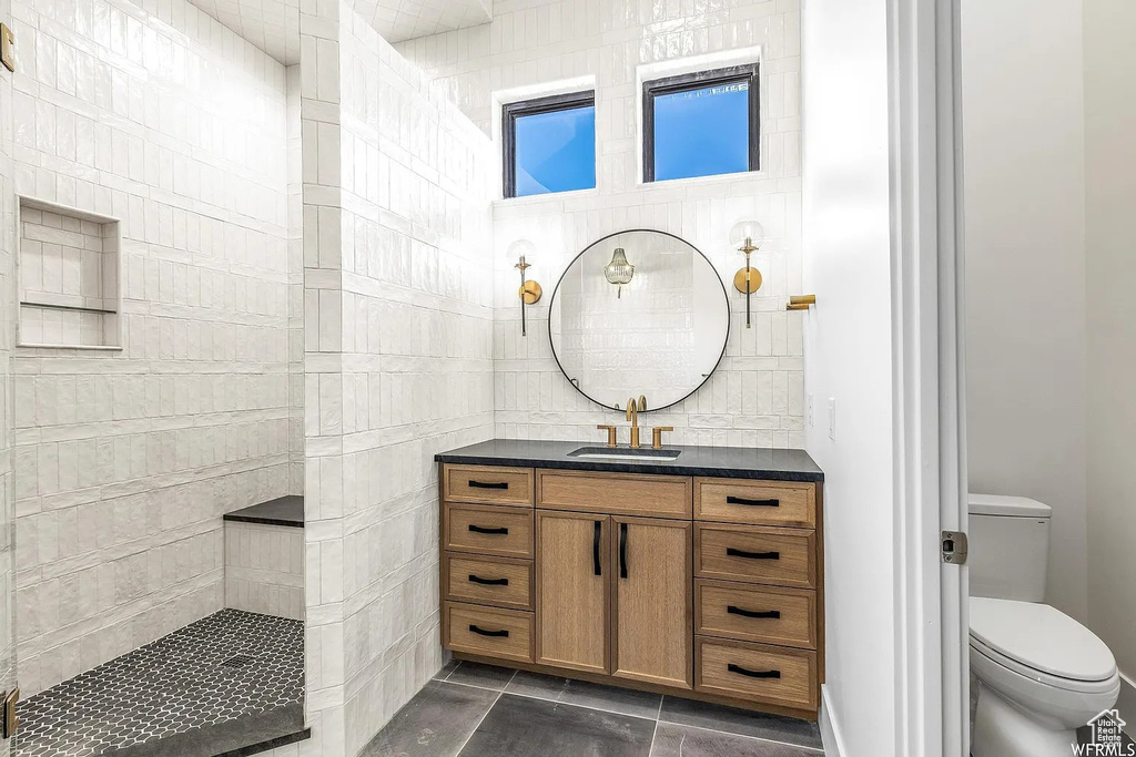 Bathroom with tile flooring, toilet, a tile shower, and vanity