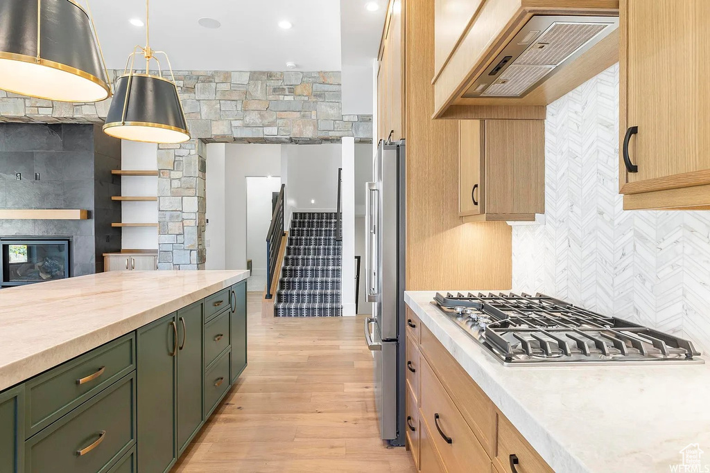 Kitchen with appliances with stainless steel finishes, light wood-type flooring, custom range hood, green cabinets, and pendant lighting