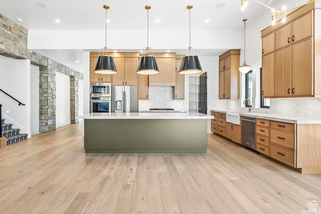Kitchen with a center island, decorative light fixtures, light wood-type flooring, and stainless steel appliances