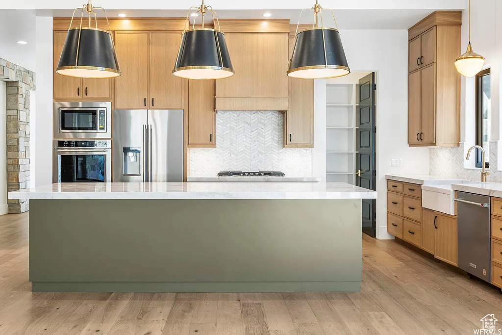 Kitchen featuring stainless steel appliances, decorative light fixtures, a kitchen island, tasteful backsplash, and light hardwood / wood-style flooring