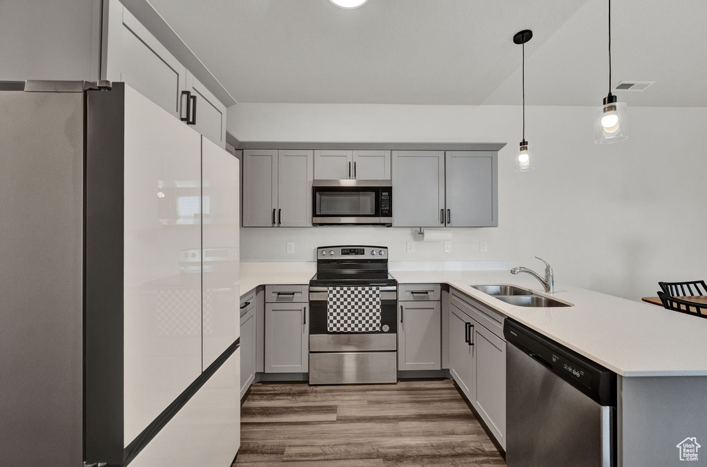 Kitchen featuring gray cabinetry, hanging light fixtures, stainless steel appliances, and hardwood / wood-style floors