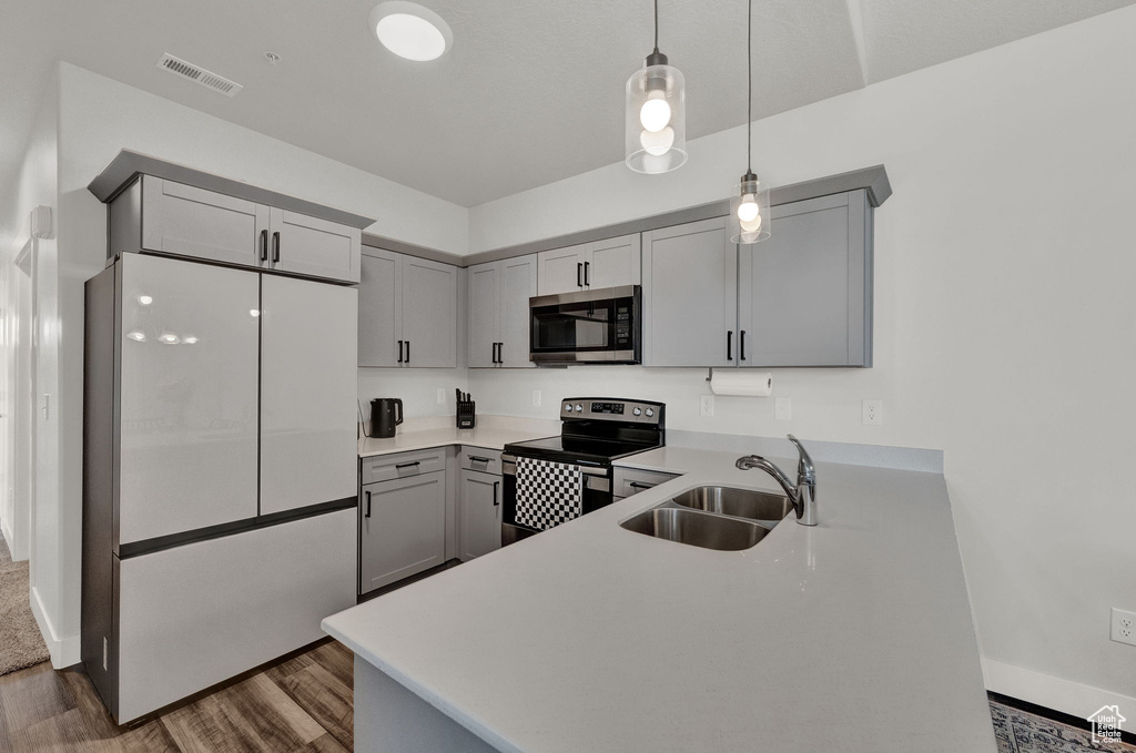 Kitchen featuring dark hardwood / wood-style floors, stainless steel appliances, gray cabinets, pendant lighting, and sink