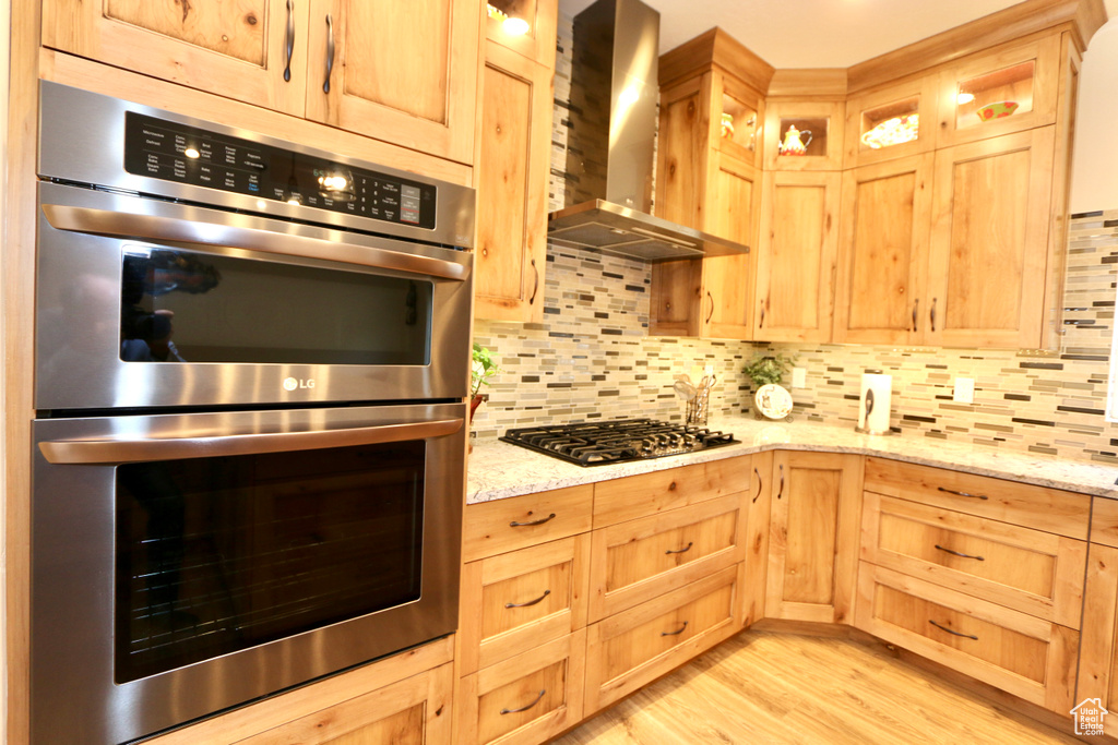 Kitchen featuring backsplash, double oven, light hardwood / wood-style floors, wall chimney range hood, and gas cooktop