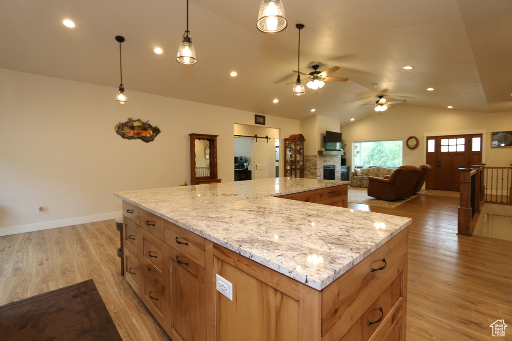 Kitchen featuring hanging light fixtures, ceiling fan, light wood-type flooring, a kitchen island, and a stone fireplace