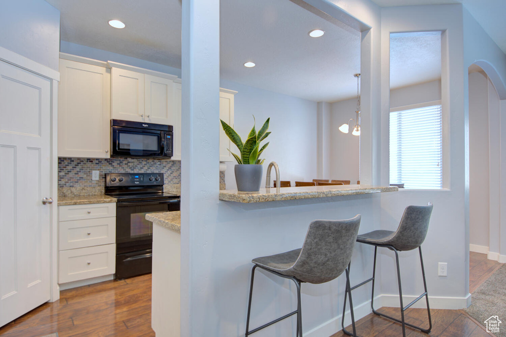 Kitchen with hanging light fixtures, backsplash, dark hardwood / wood-style floors, black appliances, and white cabinets