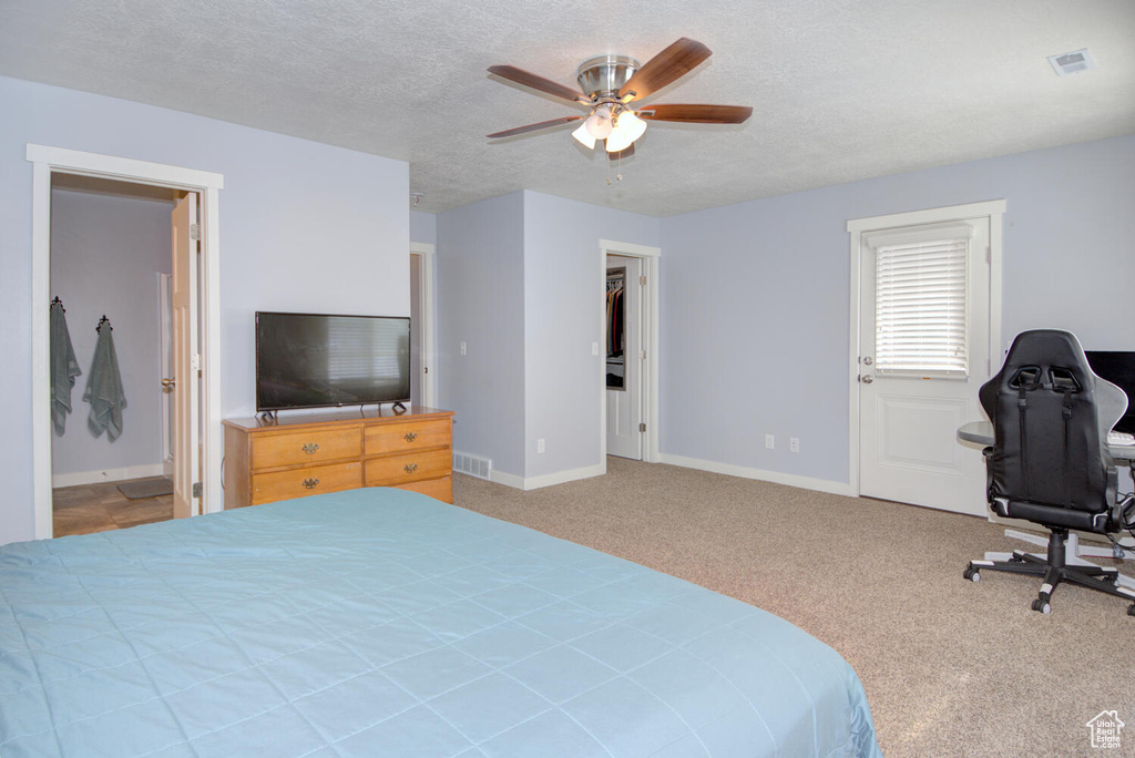 Carpeted bedroom featuring a textured ceiling, a spacious closet, ceiling fan, and ensuite bathroom