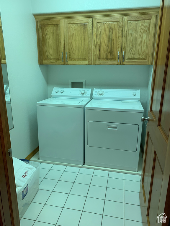 Clothes washing area with cabinets, light tile flooring, and washer and clothes dryer