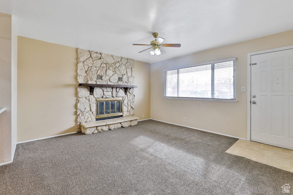 Unfurnished living room featuring ceiling fan, dark colored carpet, and a fireplace